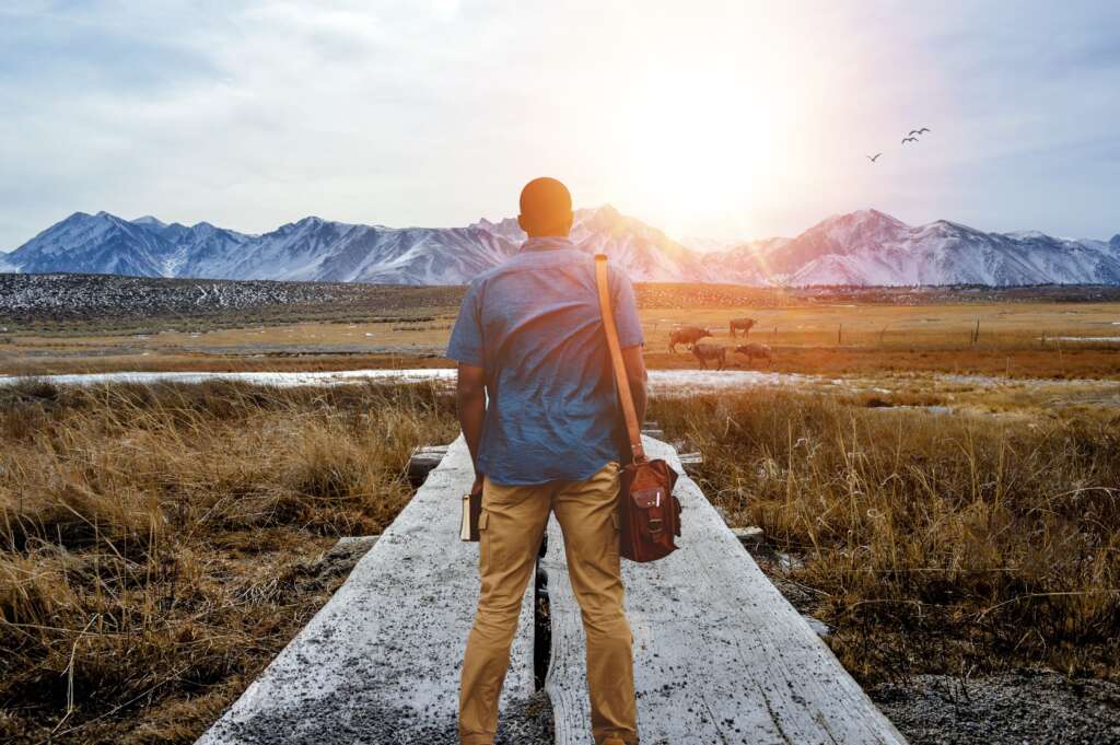 Man standing on a path leading towards vast mountains under a hopeful sunrise, symbolizing the journey of recovery from addiction.