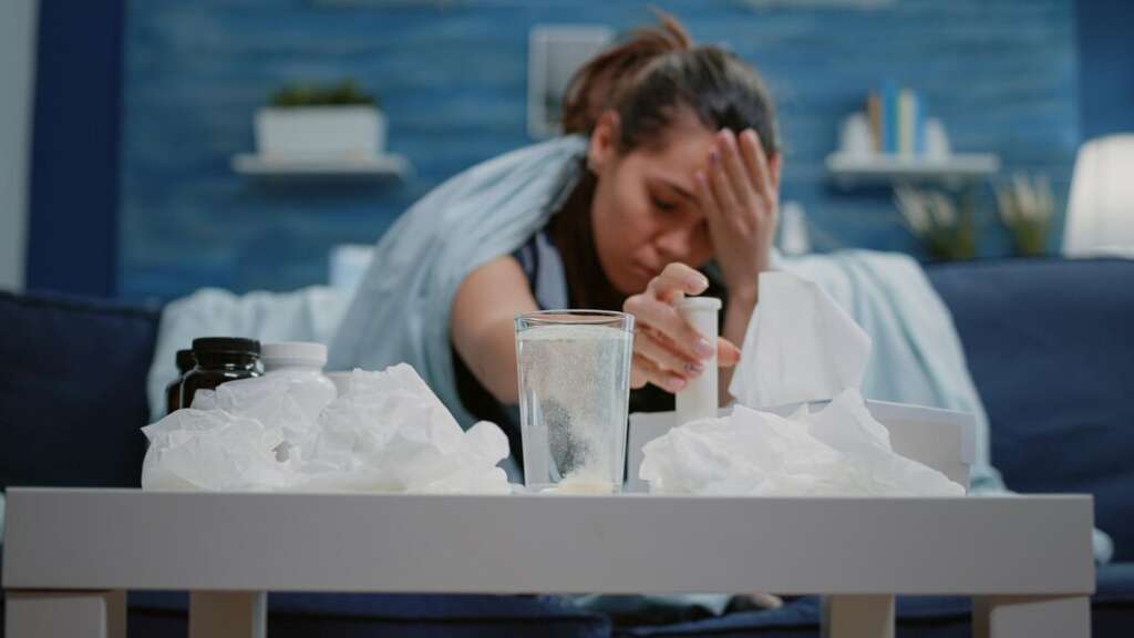 Woman suffering on a couch with medications and tissues on the table, showing signs of withdrawal or illness.
