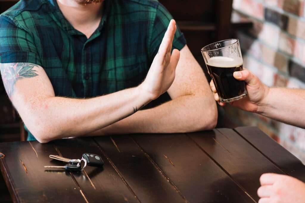 Man refusing a glass of beer with a hand gesture of stop, showing alcohol refusal and self-control.